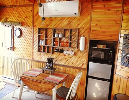 Cozy wooden interior of a cabin featuring a dining table, kitchenette, and air conditioning unit.