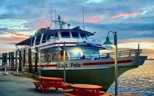 A boat named "Capt. Pete" docked at a pier during sunset, with colorful skies and picnic tables nearby.