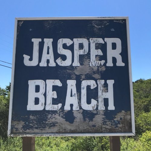Sign for Jasper Beach against a clear blue sky, with weathered white letters on a blue background.