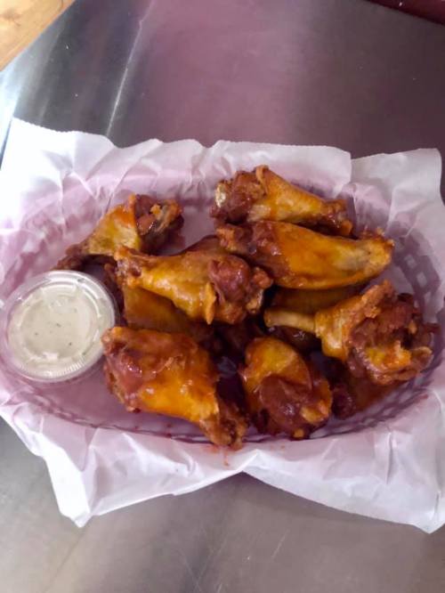 A basket of crispy chicken wings with a side of dipping sauce on a paper-lined tray.