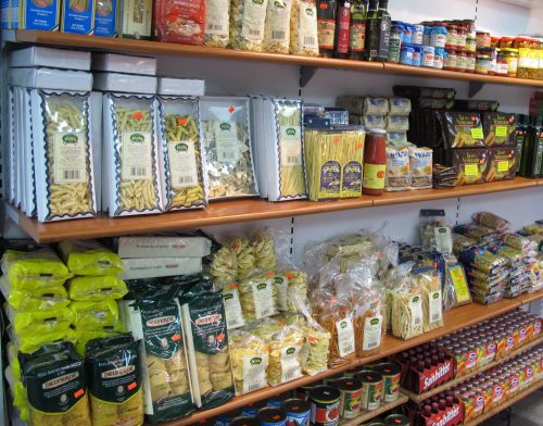 A grocery shelf filled with various pasta, sauces, and canned goods in organized packaging.