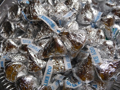 A close-up of numerous Hershey's Kisses wrapped in silver foil with blue messages on the paper strips.