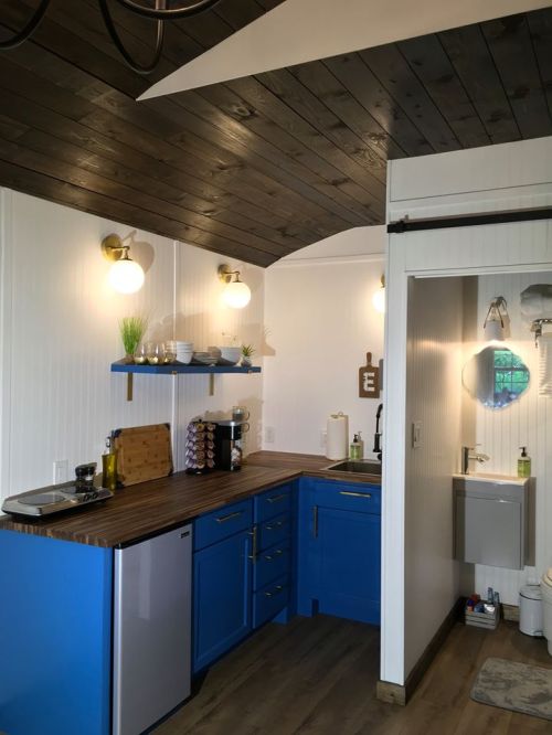 A modern kitchen with blue cabinets, wooden countertops, and stylish lighting, featuring a small sink and appliances.