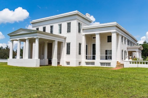 A large white historic building with columns, set against a blue sky and green grass.