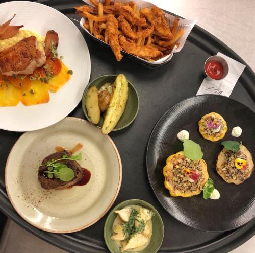 A tray with four gourmet dishes: chicken with vegetables, sweet potato fries, a meat dish, and colorful appetizers.
