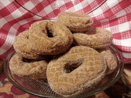 A glass plate stacked with cinnamon sugar-coated donuts, set against a red and white checkered cloth.