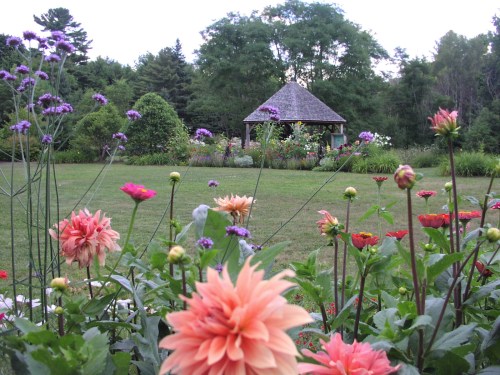 A vibrant garden filled with colorful flowers in the foreground, leading to a gazebo surrounded by lush greenery.