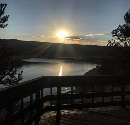 Sunset over a calm lake, with rays of light reflecting on the water and trees framing the view.