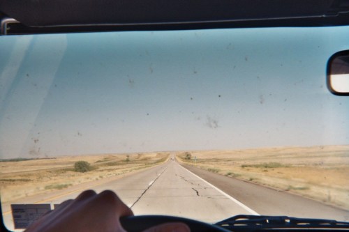 A view from inside a vehicle, showing a long, straight road stretching into the horizon under a clear sky.