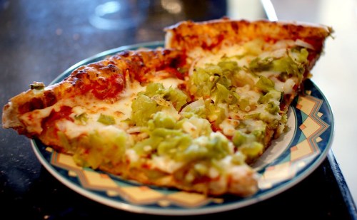 Two slices of pizza on a decorative plate, topped with cheese and green peppers.