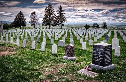 A serene cemetery with rows of white gravestones under a cloudy sky, featuring a prominent headstone with an American flag.
