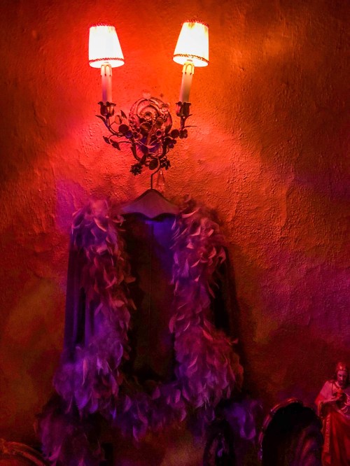 A wall adorned with a vintage sconce and a feather boa, illuminated by warm, colorful lighting.