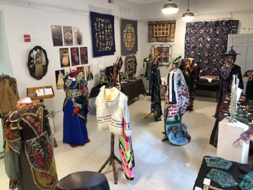 A vibrant exhibition room displaying various colorful garments and textile art on mannequins and walls.