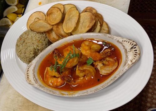 A dish featuring shrimp in a spicy sauce, served with rice and crispy potato slices on a white plate.
