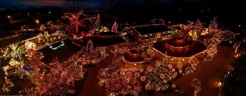 Aerial view of a festive display with numerous colorful lights adorning trees and buildings at night.