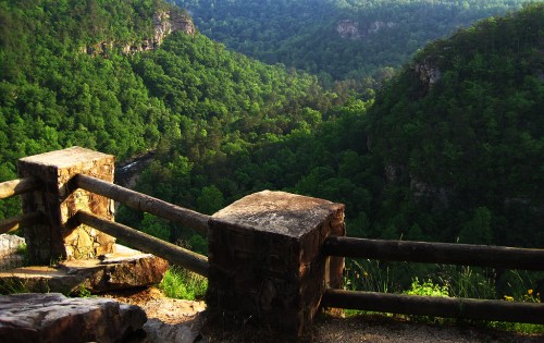 A scenic view of lush green valleys and hills, framed by a rustic wooden fence in the foreground.