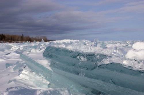 A landscape of jagged, translucent ice formations against a cloudy sky, with a snowy ground in the foreground.