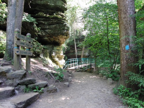 A forested path leads to a bridge, with signs for a visitor center and nearby attractions in a natural setting.