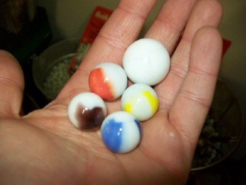 A hand holding five colorful marbles in various sizes, featuring swirls of red, blue, yellow, and brown.