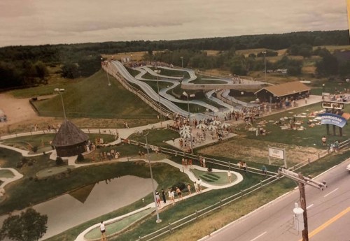 Aerial view of a water park with slides, a mini-golf area, and visitors enjoying the attractions on a cloudy day.