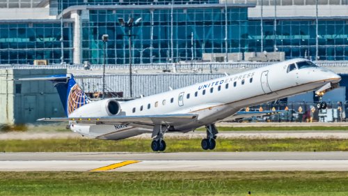 A United Express regional jet taking off with a clear blue sky and airport buildings in the background.