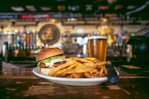 A juicy burger with toppings and a side of golden fries, accompanied by a glass of beer on a rustic wooden table.