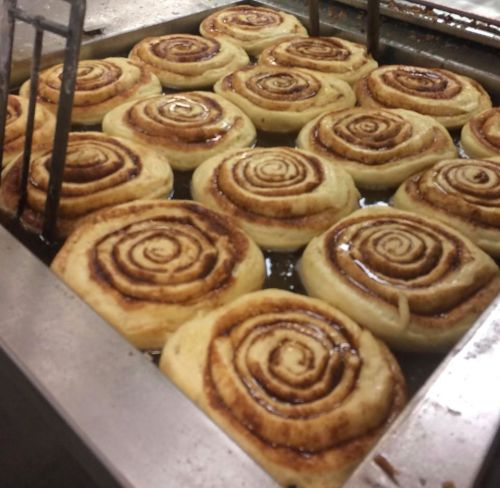 Freshly baked cinnamon rolls cooling in a tray, glistening with syrup and showcasing their spiral layers.