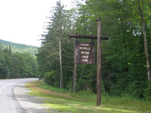 Sign for Dixville Notch State Park along a tree-lined road, indicating entrance to the park.