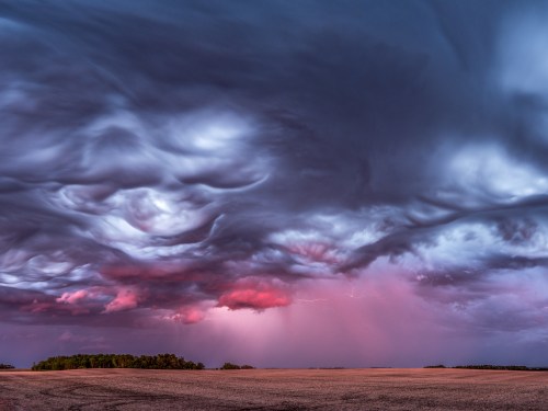 Dramatic sky with swirling clouds and hints of pink, illuminated by distant lightning over a vast, open landscape.