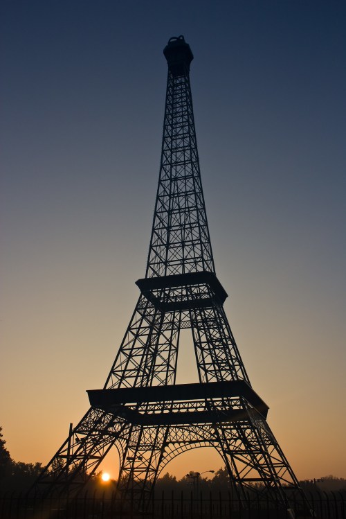 Silhouette of the Eiffel Tower against a sunrise sky, with warm hues illuminating the scene.