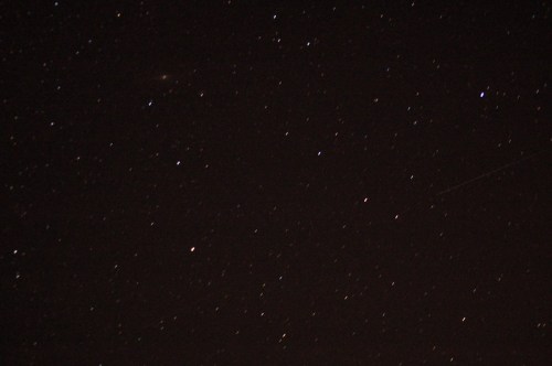 A night sky filled with stars, including a few bright points and a faint streak, possibly a meteor or satellite.