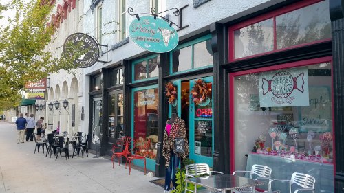 A colorful storefront with signs for a coffee shop and candy store, featuring outdoor seating and autumn decorations.