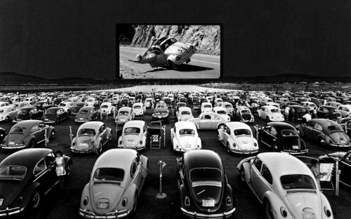 A vintage drive-in theater scene with rows of cars facing a large screen showing a movie.