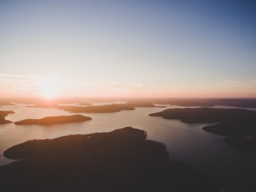 Aerial view of a serene lake at sunset, with islands scattered across the water and a colorful sky.