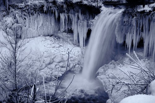 A frozen waterfall surrounded by icicles and snow-covered trees, creating a serene winter landscape.