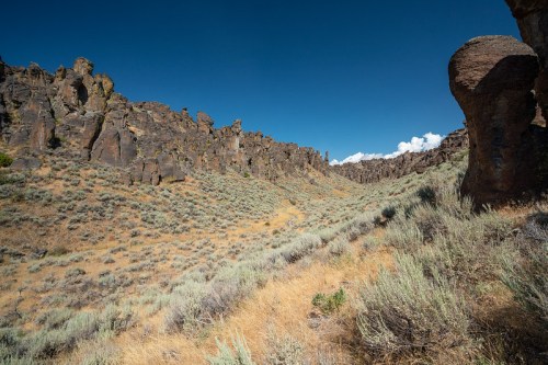 A rugged canyon landscape with rocky cliffs and sparse vegetation under a clear blue sky.