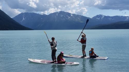 Three people paddleboarding on a calm lake with mountains in the background under a partly cloudy sky.