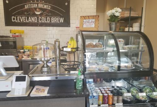 A coffee shop counter with a display case of pastries, drinks, and a sign for Cleveland Cold Brew.