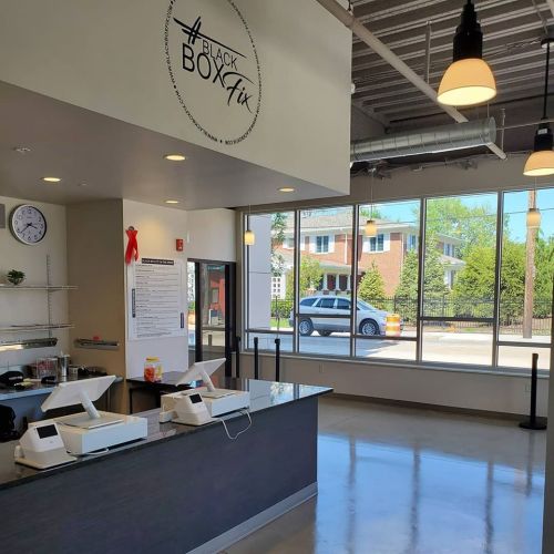 Interior of a modern cafe with a counter, menu board, and large windows showing a street view outside.