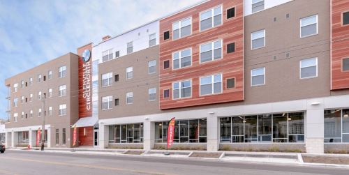 Modern multi-story building with a mix of brick and wood paneling, featuring large windows and a welcoming entrance.
