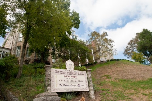 Sign for the Historic Crescent Hotel, featuring the spa and dining room, with a hillside and trees in the background.