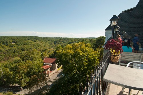 A scenic view from a balcony overlooking lush green hills and a distant road, with people enjoying the outdoors.