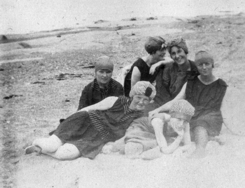 A vintage black-and-white photo of six women in swimsuits and headscarves, posing on a beach.