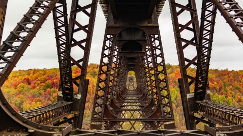 View of a metal bridge structure with repeating arches, framed by colorful autumn foliage in the background.