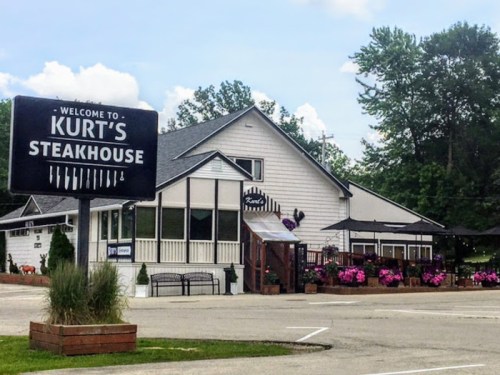 A welcoming sign for Kurt's Steakhouse in front of a charming building with outdoor seating and colorful flowers.