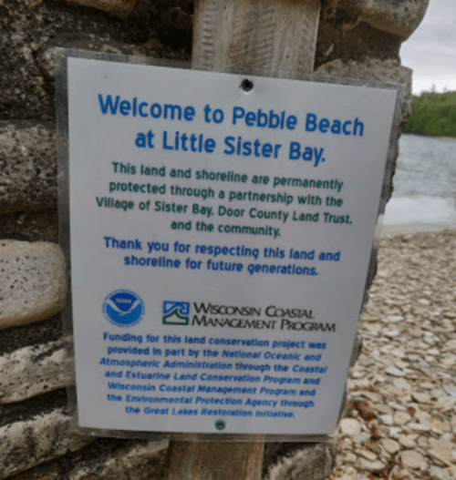 Sign at Pebble Beach, Little Sister Bay, highlighting land conservation efforts and community partnership.