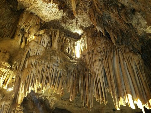 Stalactites and stalagmites in a dimly lit cave, showcasing intricate rock formations and textures.