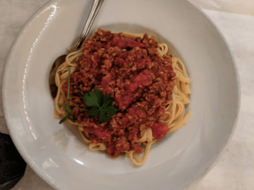 A bowl of spaghetti topped with a rich meat sauce and garnished with a sprig of parsley.