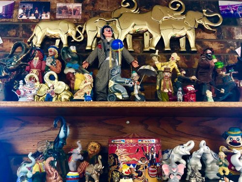 A colorful display of various figurines, including elephants, clowns, and a woman in traditional attire, on a wooden shelf.