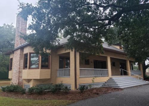 A charming yellow house with a brick chimney, surrounded by trees and featuring a front porch and steps.